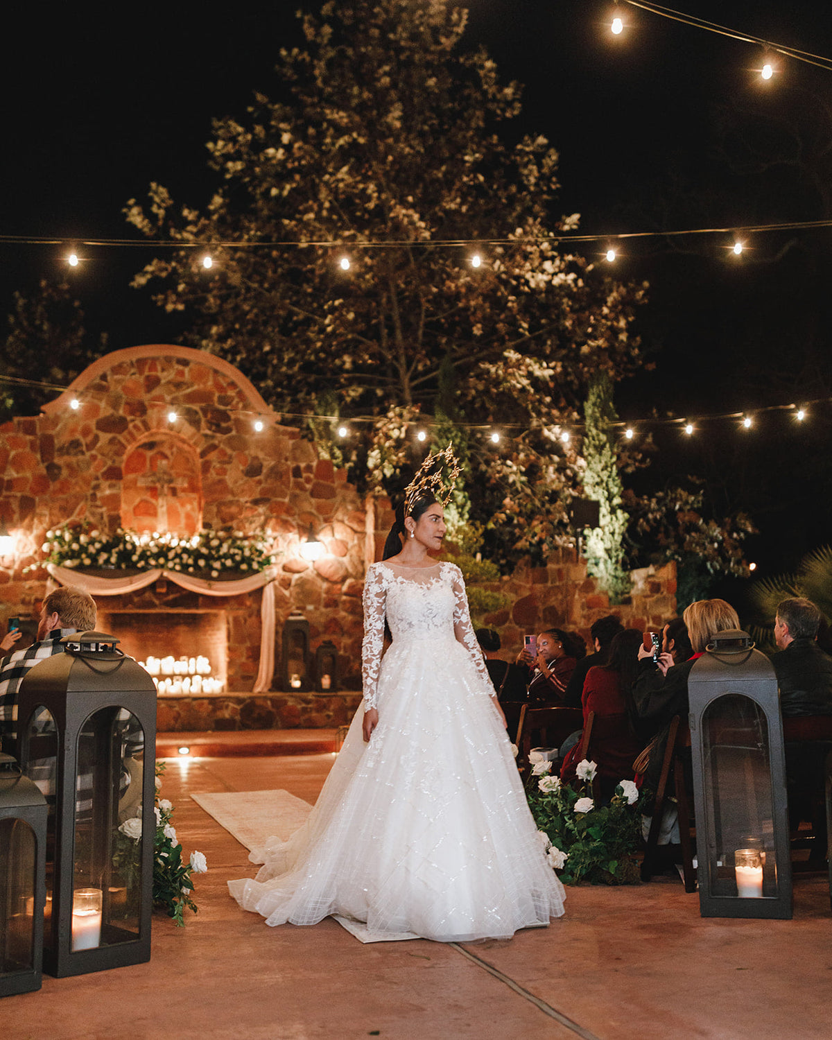 Bride in custom lace wedding gown at outdoor night ceremony with string lights and stone arch