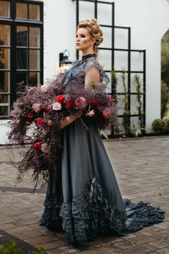 Bride in dark lace wedding gown with dramatic train, holding oversized burgundy floral bouquet, gothic bridal style