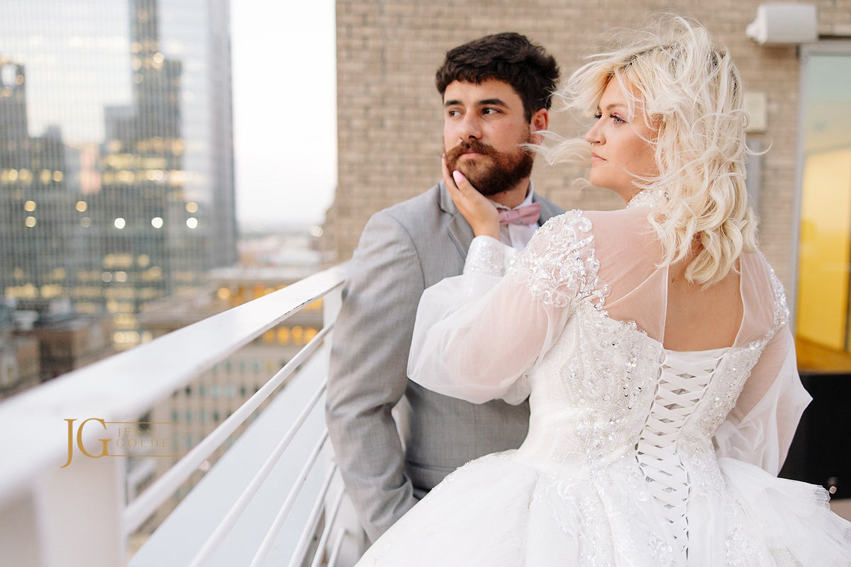 Bride in custom beaded wedding gown with lace-up back, groom in gray suit, city skyline backdrop