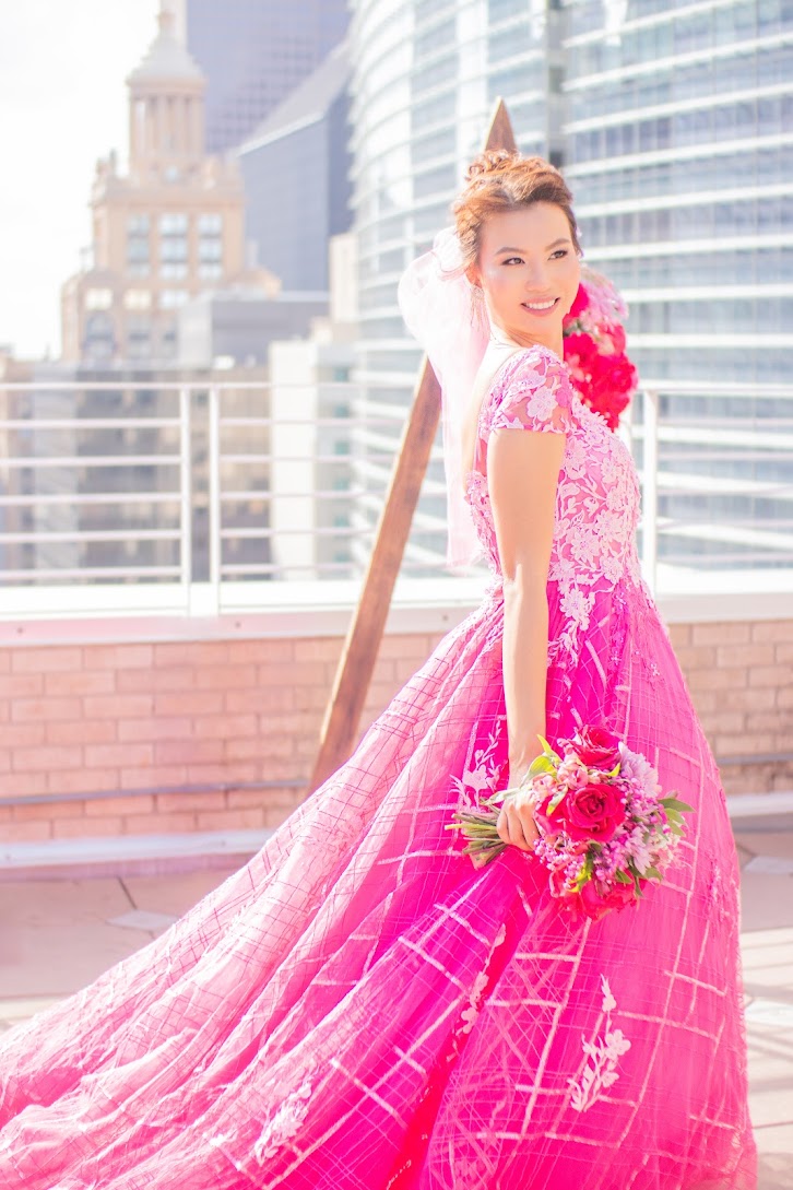 Vibrant pink custom wedding dress with lace and grid pattern, rooftop cityscape, bridal bouquet