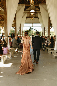 Bride in custom embroidered wedding dress walking down aisle with groom at rustic barn venue