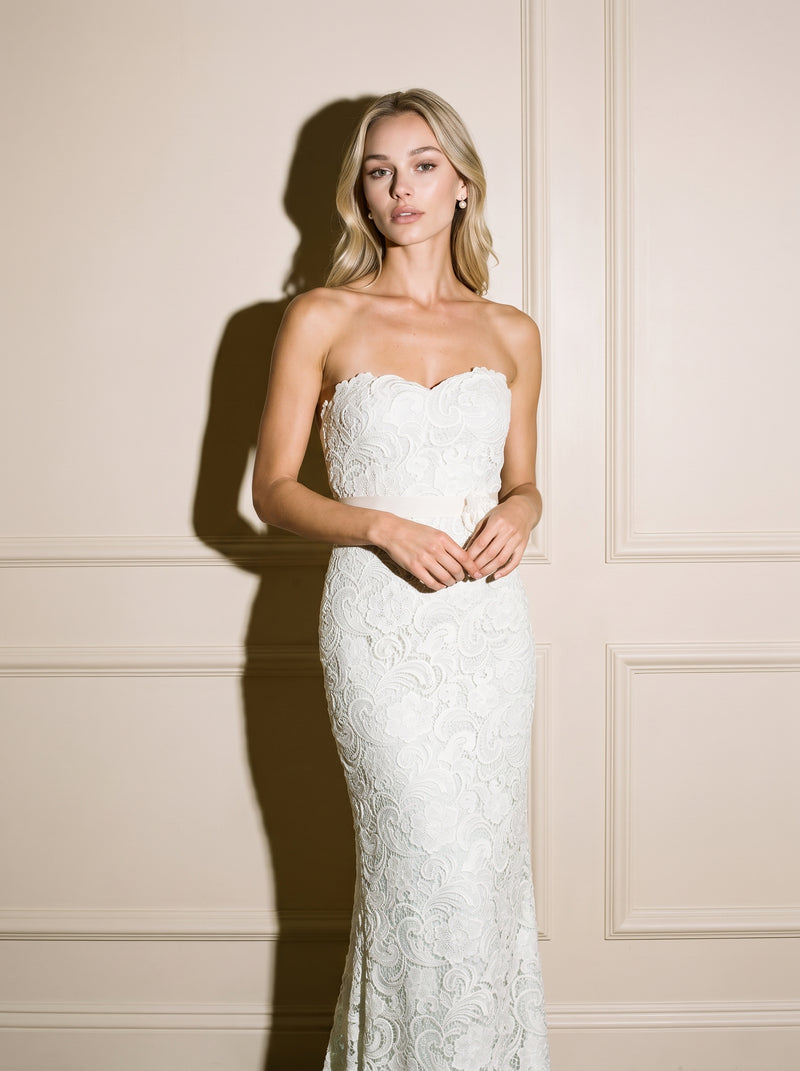 A woman modeling a strapless white lace mermaid-style gown