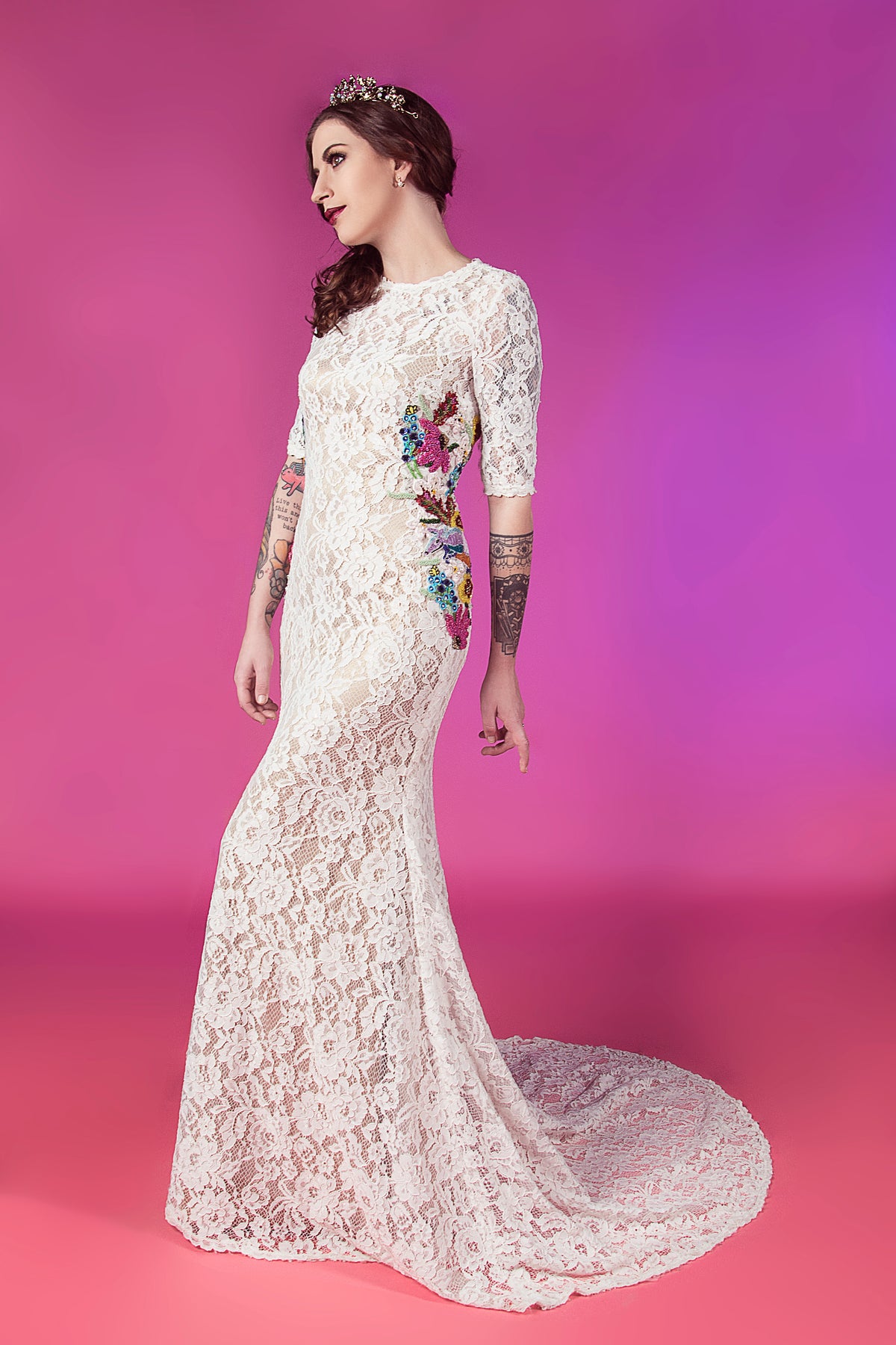 White lace mermaid wedding dress with colorful floral embroidery, 3/4 sleeves, and train, worn by tattooed bride with tiara