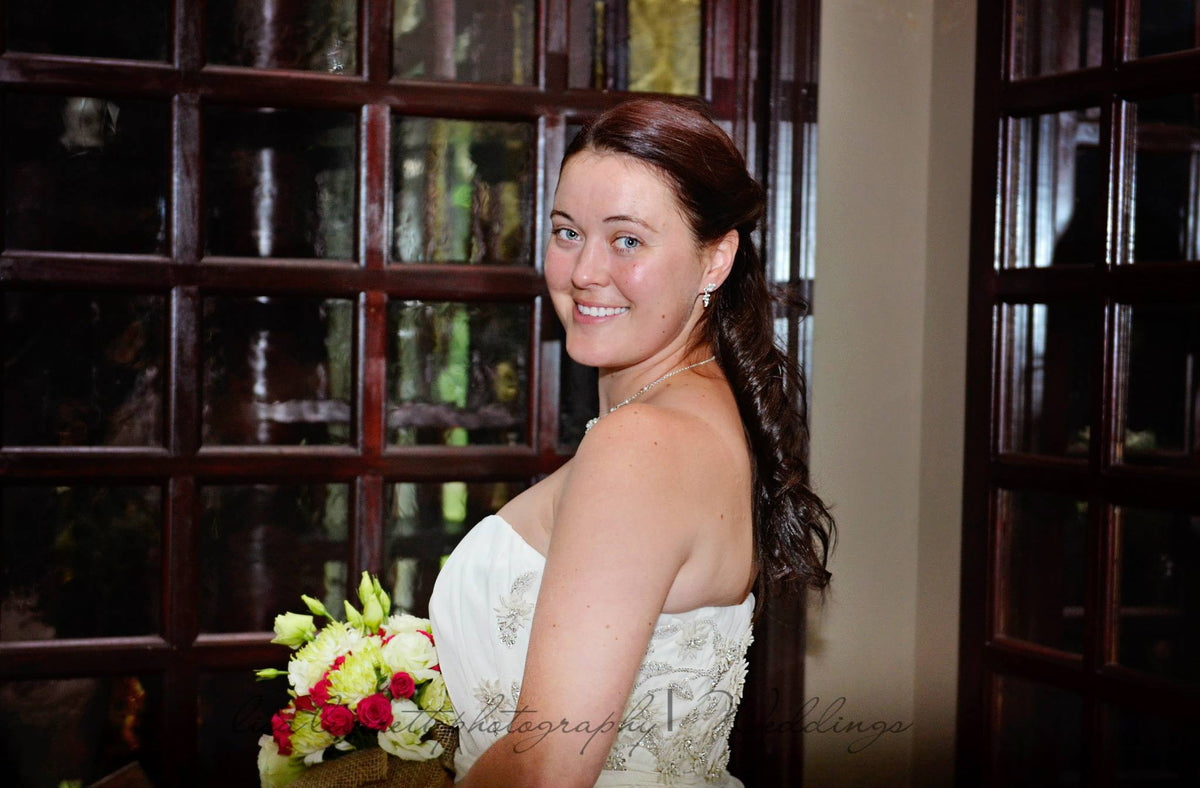 Bride in strapless wedding dress holding bouquet, elegant indoor setting with wooden windows