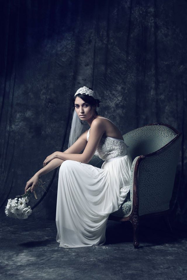 Bride in elegant white gown with lace bodice, holding daisies, seated on vintage chair