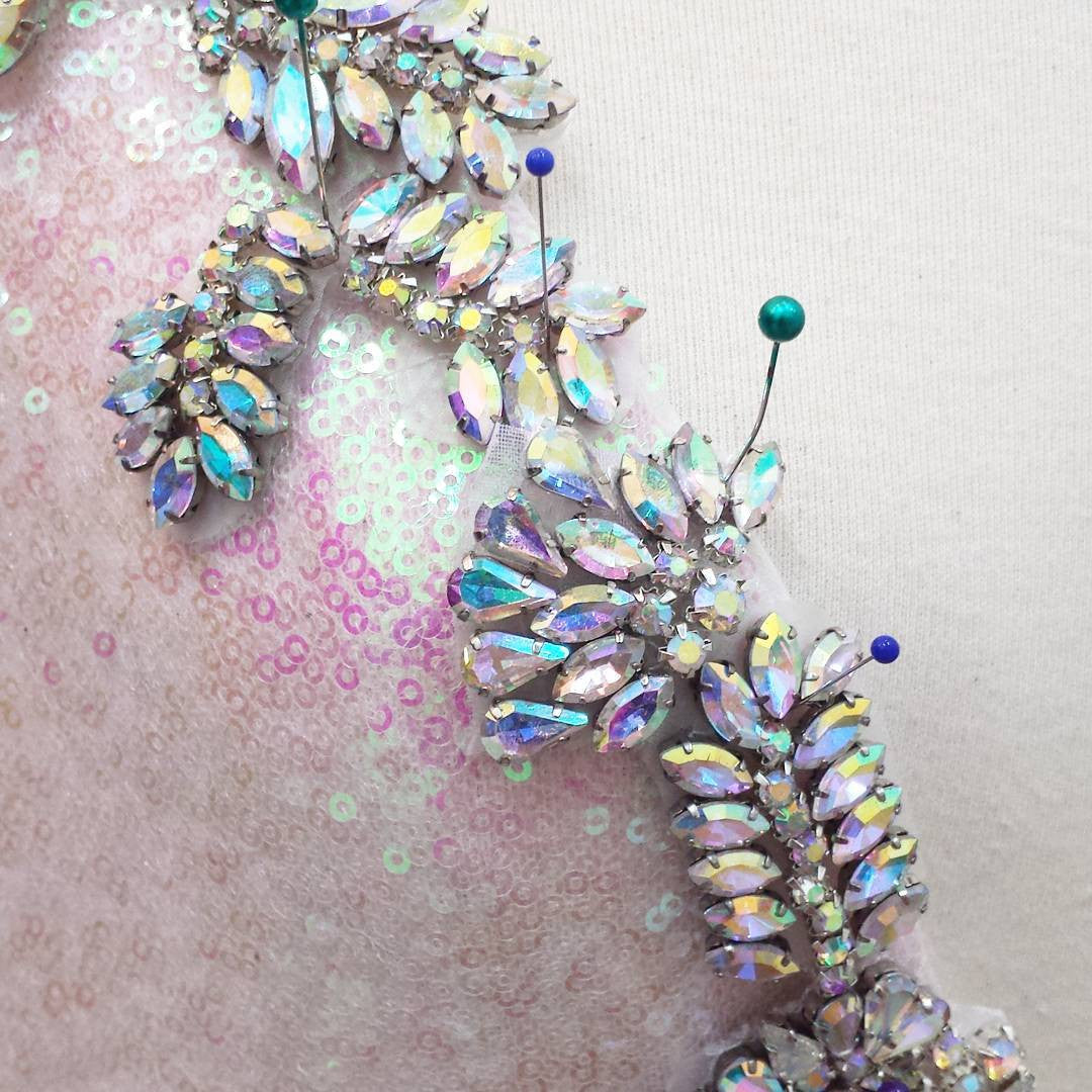 Iridescent crystal embellishments on sequined bridal fabric, pinned for custom design