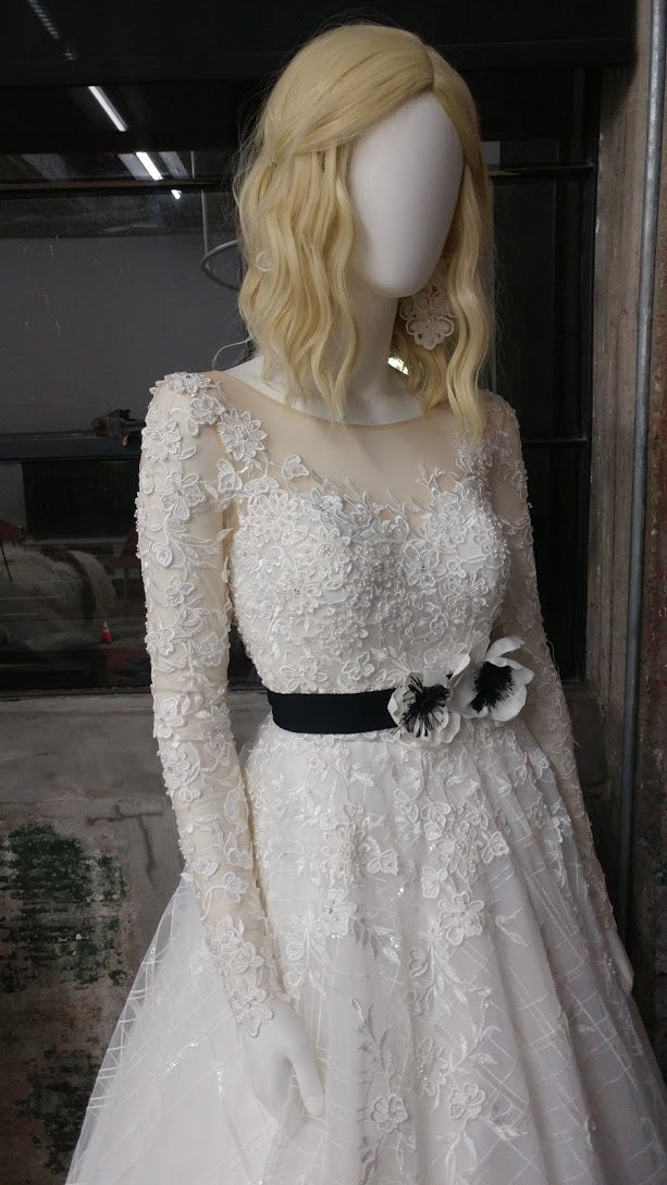 Elegant lace wedding dress with long sleeves and black floral belt, styled on mannequin