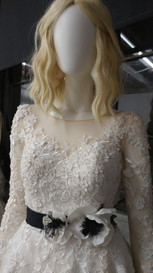 Elegant lace wedding dress with floral appliqués and black belt, styled on mannequin