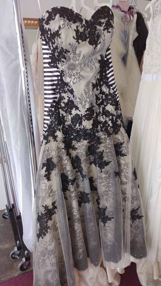 Black lace floral appliqué wedding dress with sheer overlay, displayed on rack among bridal gowns