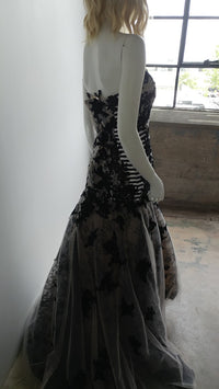 Black lace mermaid wedding dress with sheer overlay, displayed on mannequin near window