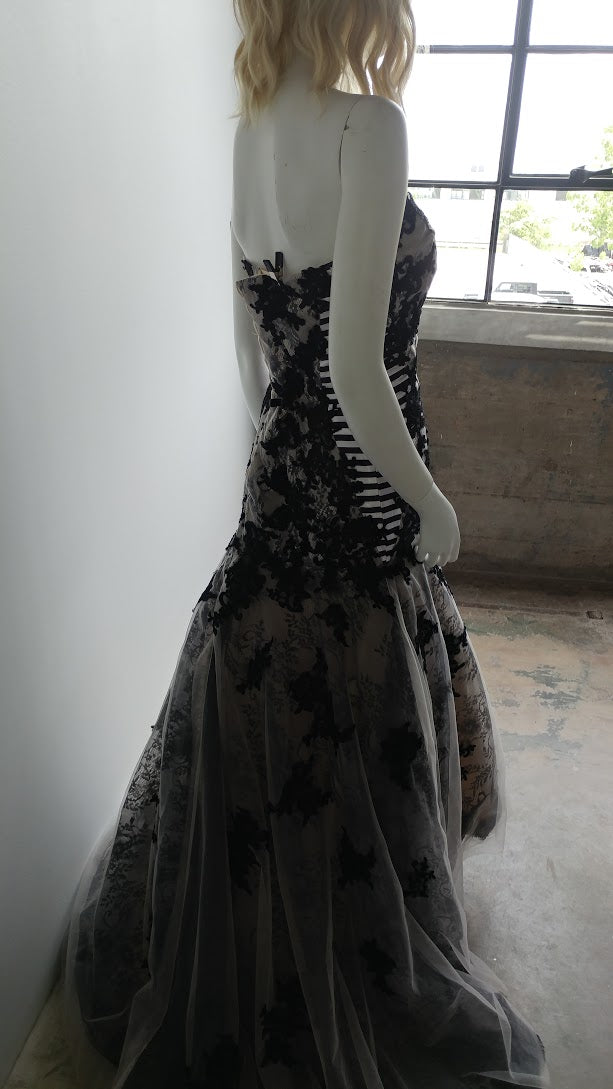 Black lace mermaid wedding dress with sheer overlay, displayed on mannequin near window