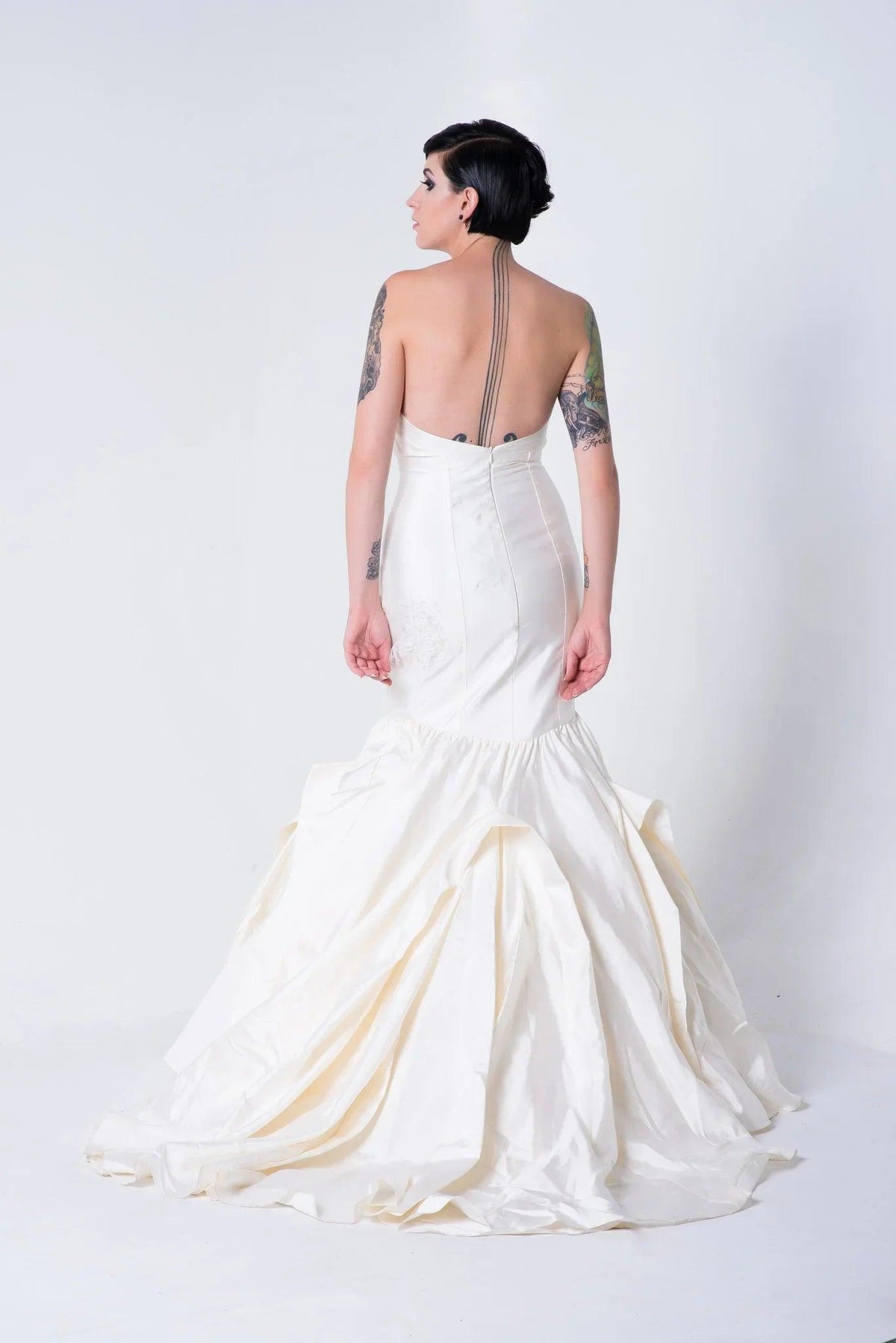 Elegant white mermaid wedding dress with open back, showcasing tattoos and luxurious train