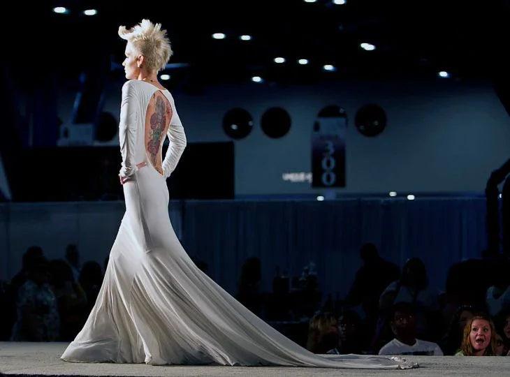 Bride in custom white wedding gown with long train and back tattoo, walking runway