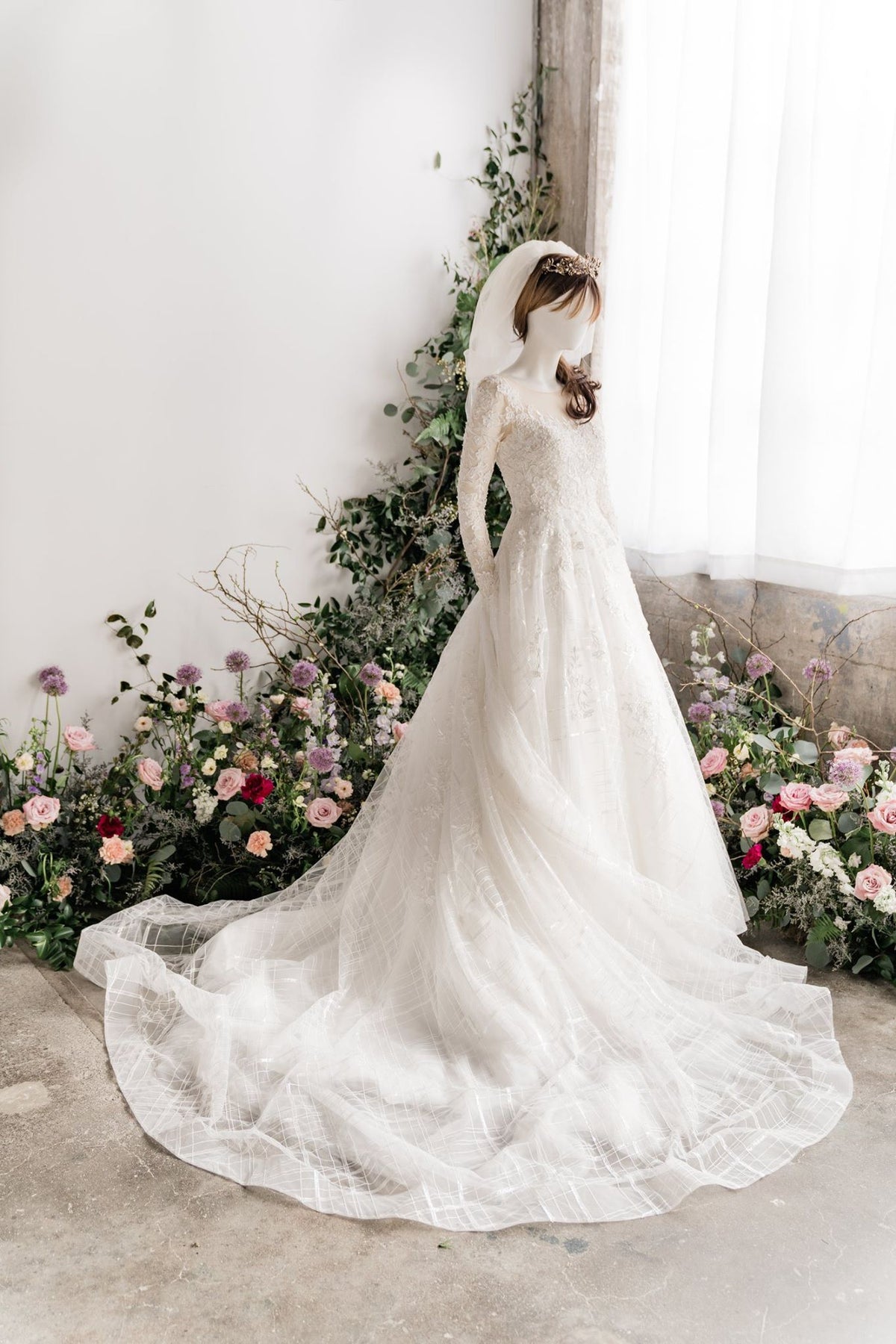 Elegant lace wedding dress with long sleeves and flowing train, surrounded by floral arrangements