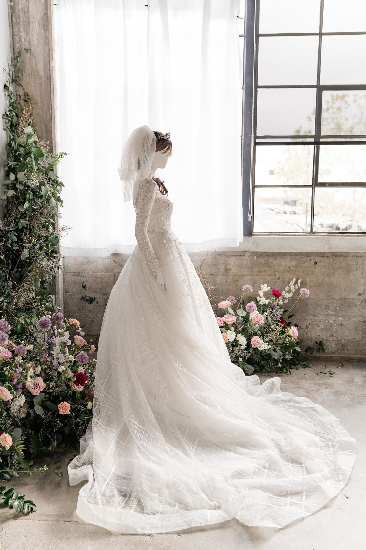 Elegant lace wedding dress with long train, veil, and floral backdrop for custom bridal design