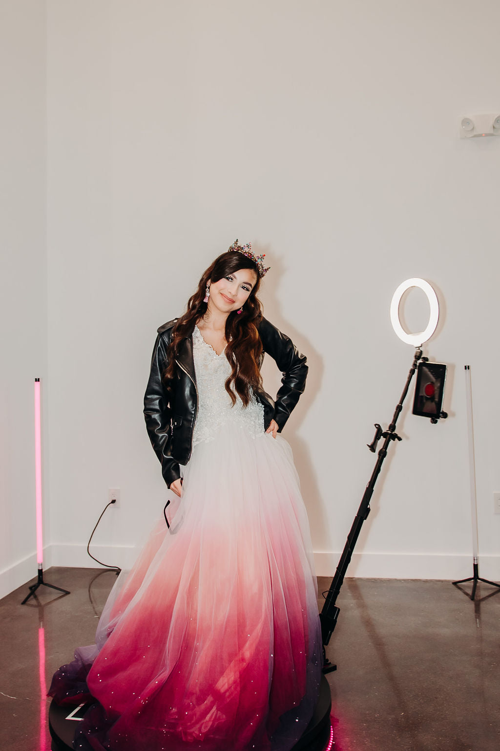 Bride in ombre pink-to-purple wedding dress with black leather jacket and tiara, studio lighting