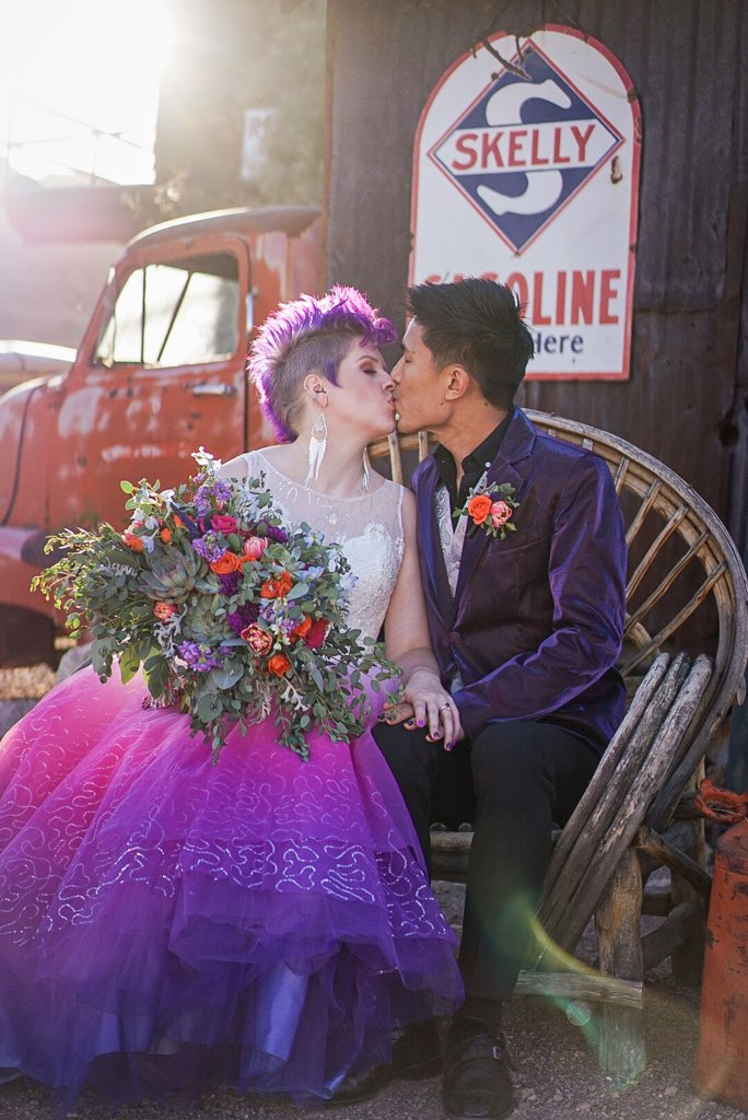 Bride in vibrant purple ombre wedding dress with groom, rustic vintage backdrop, colorful bouquet
