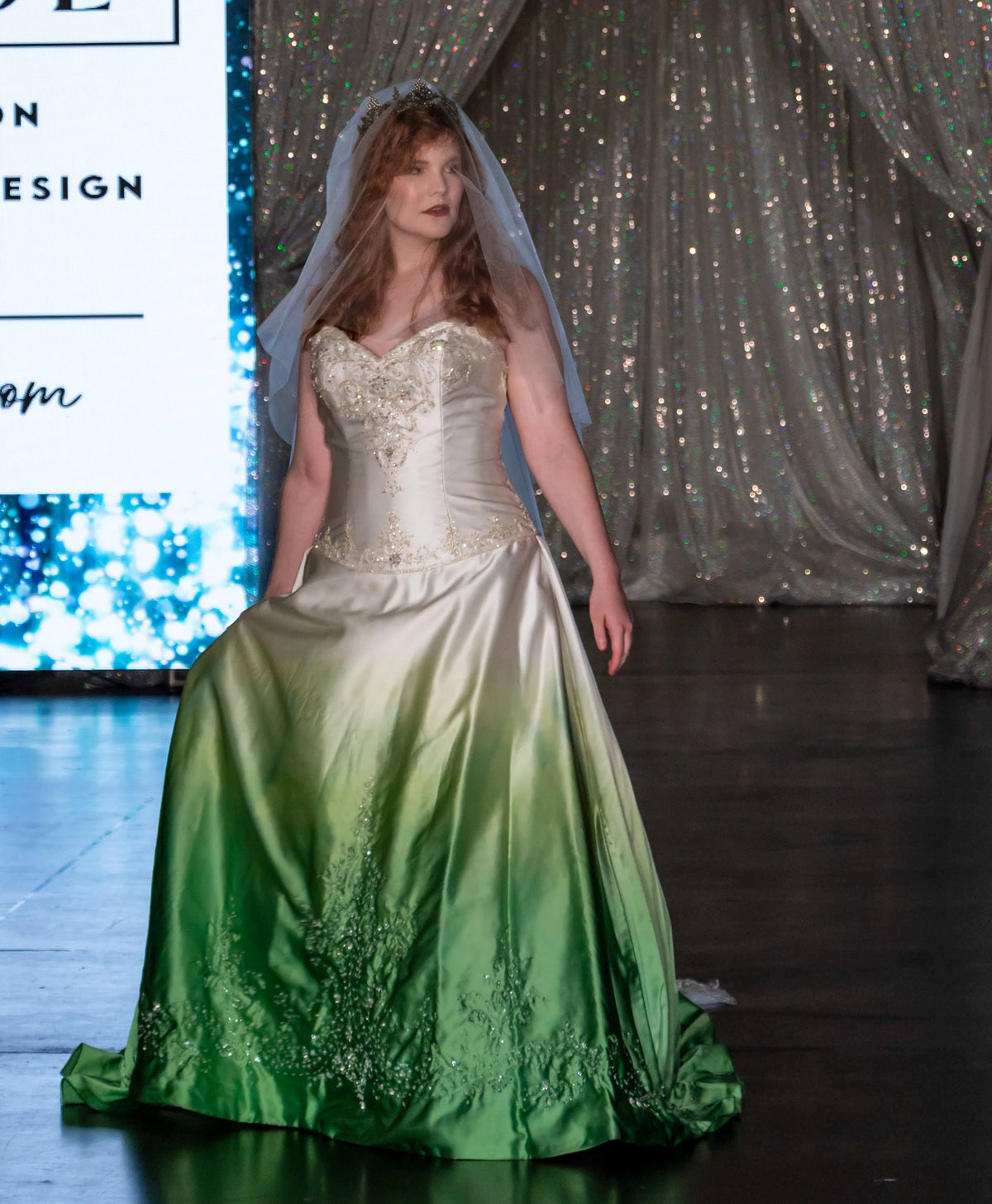 Bride in custom ombre wedding dress with green gradient skirt, beaded bodice, and veil on runway