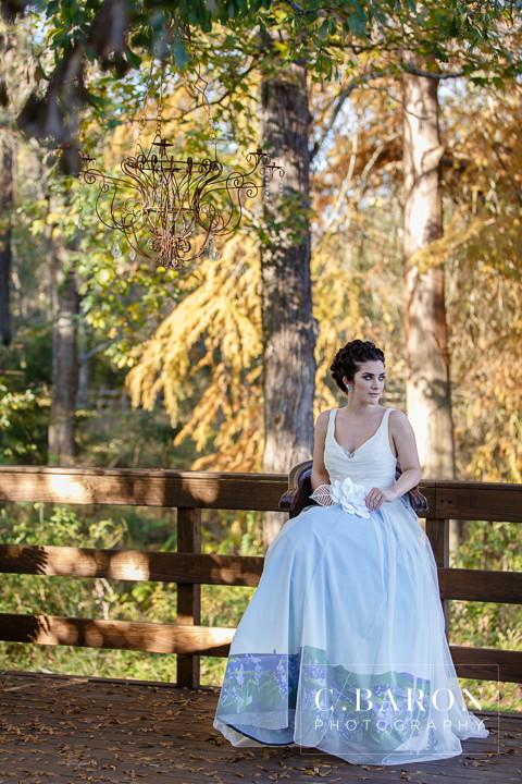 Bride in custom ombre wedding dress with floral hem, seated on rustic bridge under chandelier in autumn woods