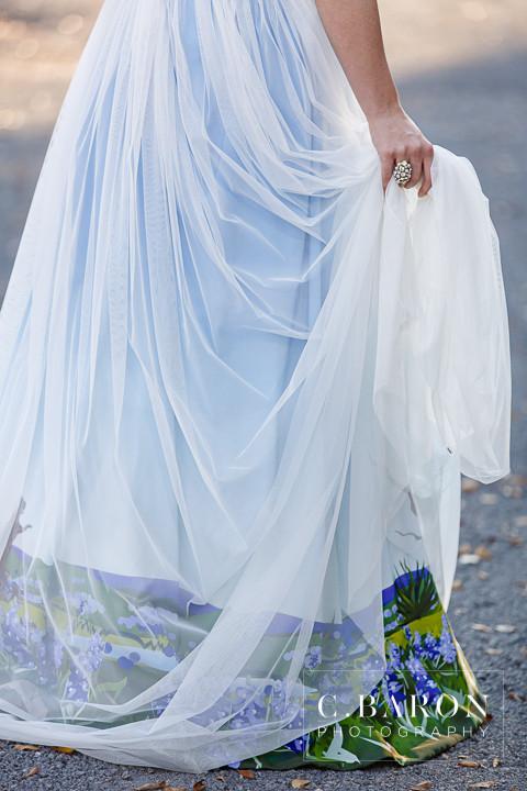 Custom wedding dress with ombre blue tulle overlay and floral print hem, held by bride outdoors