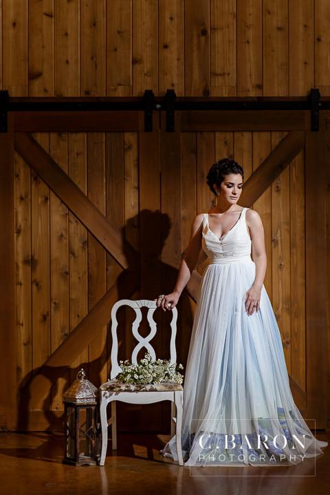 Bride in custom ombre wedding dress with lace bodice, standing beside white chair in rustic barn setting