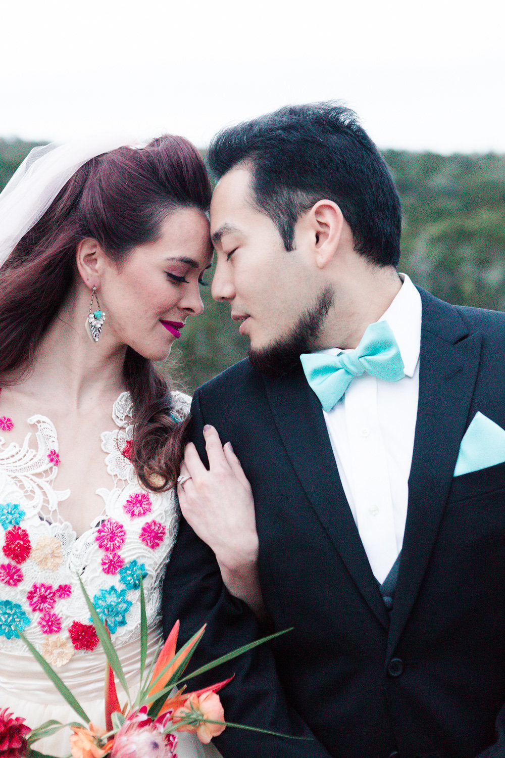 Bride in colorful floral lace wedding dress with groom in black tuxedo and mint bow tie, intimate moment outdoors