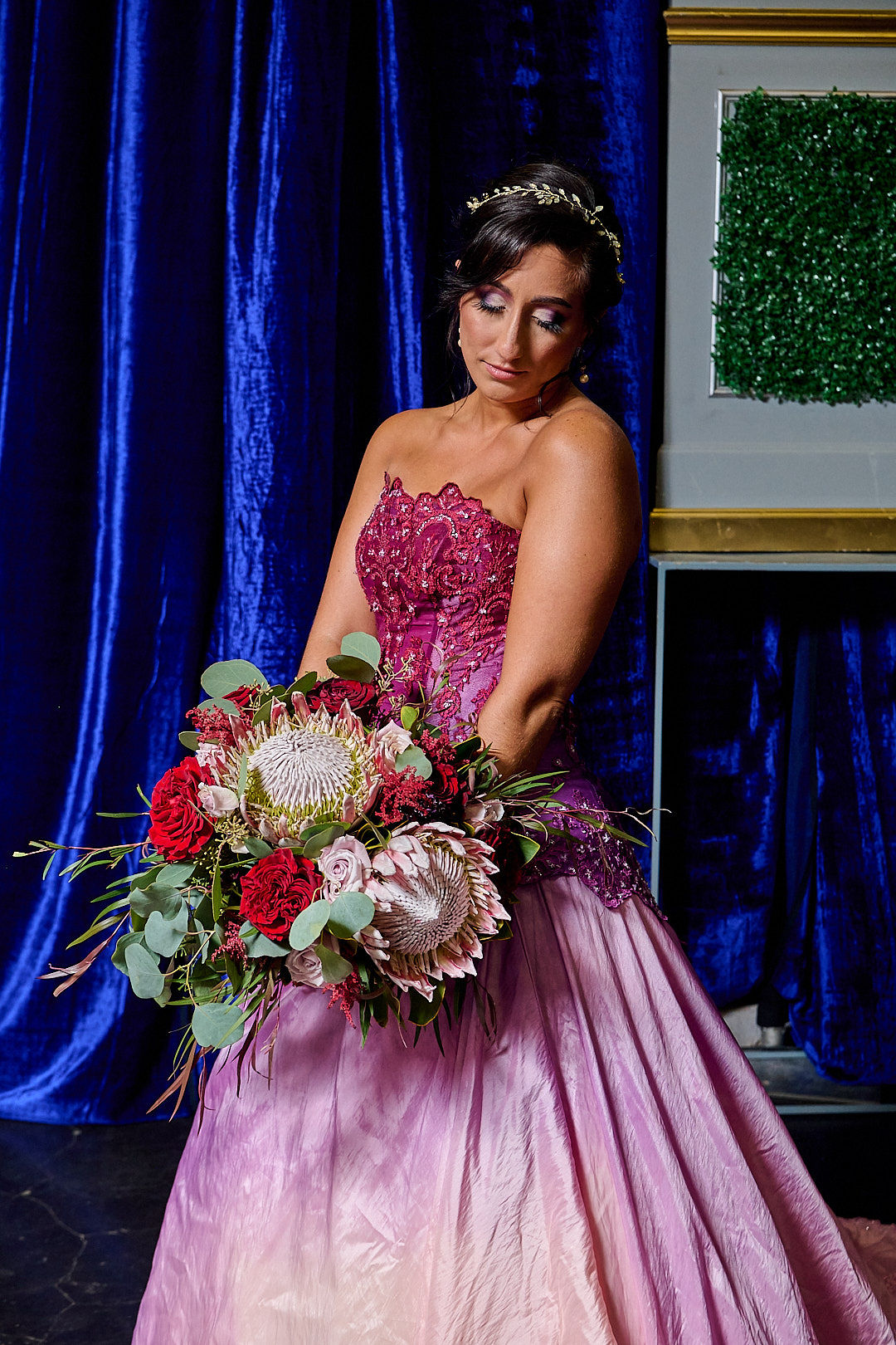 Bride in custom pink strapless wedding gown with floral bouquet, blue velvet backdrop