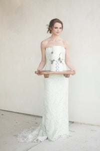 Bride in lace strapless wedding dress holding floral cake on wooden tray