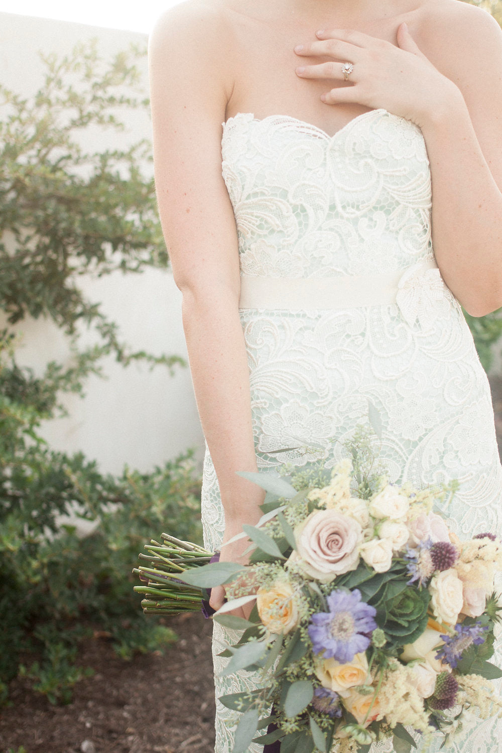 Bride in lace wedding dress holding floral bouquet, custom bridal design