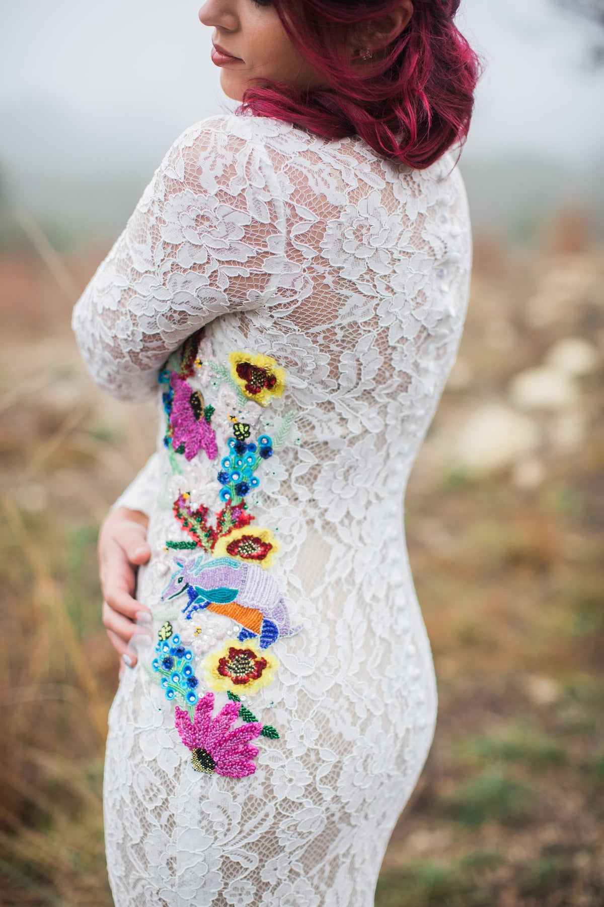 White lace wedding dress with colorful floral embroidery and armadillo detail, worn by bride with red hair