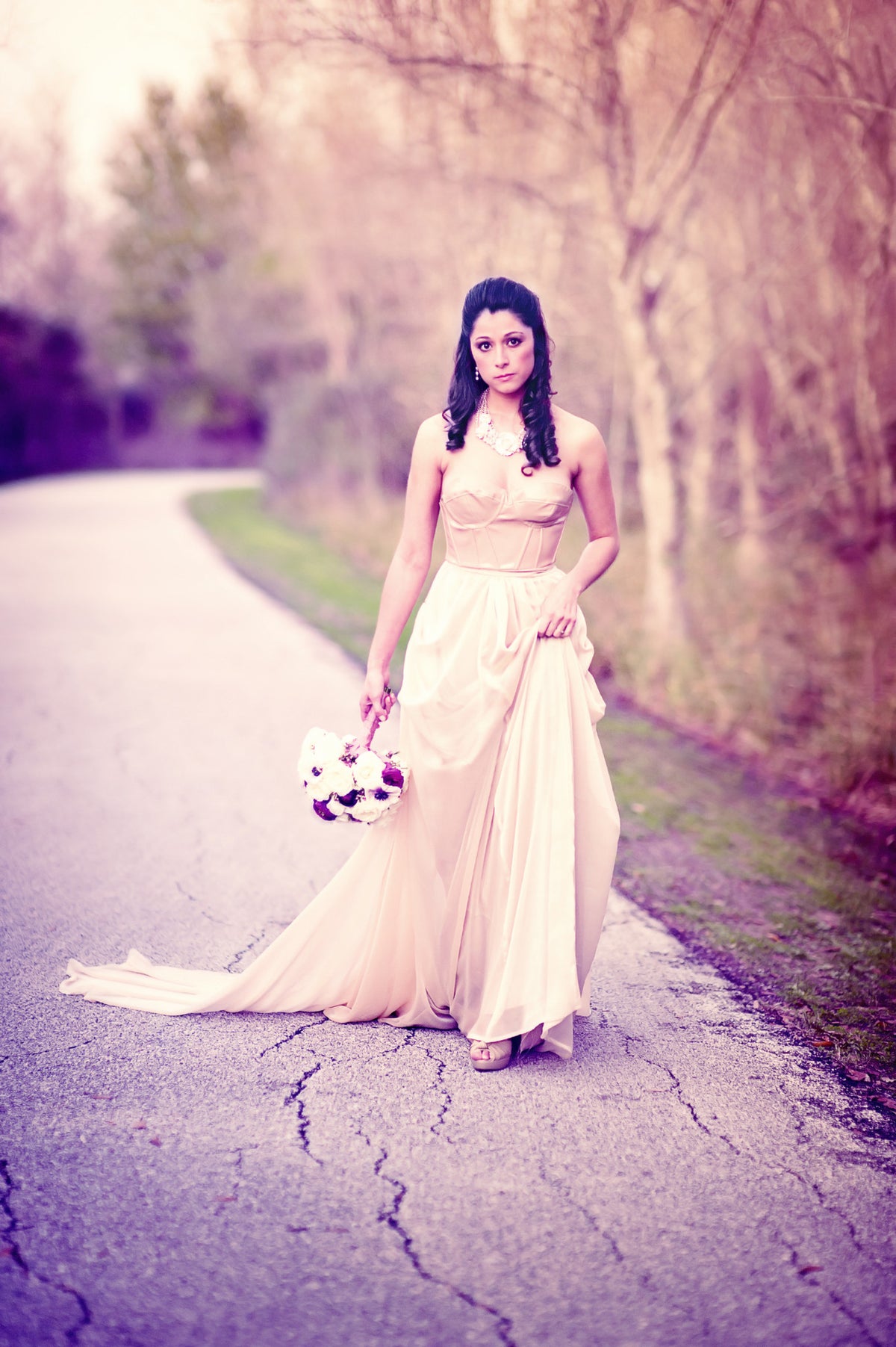 Bride in custom blush wedding gown holding bouquet on rustic path, ombre dye effect