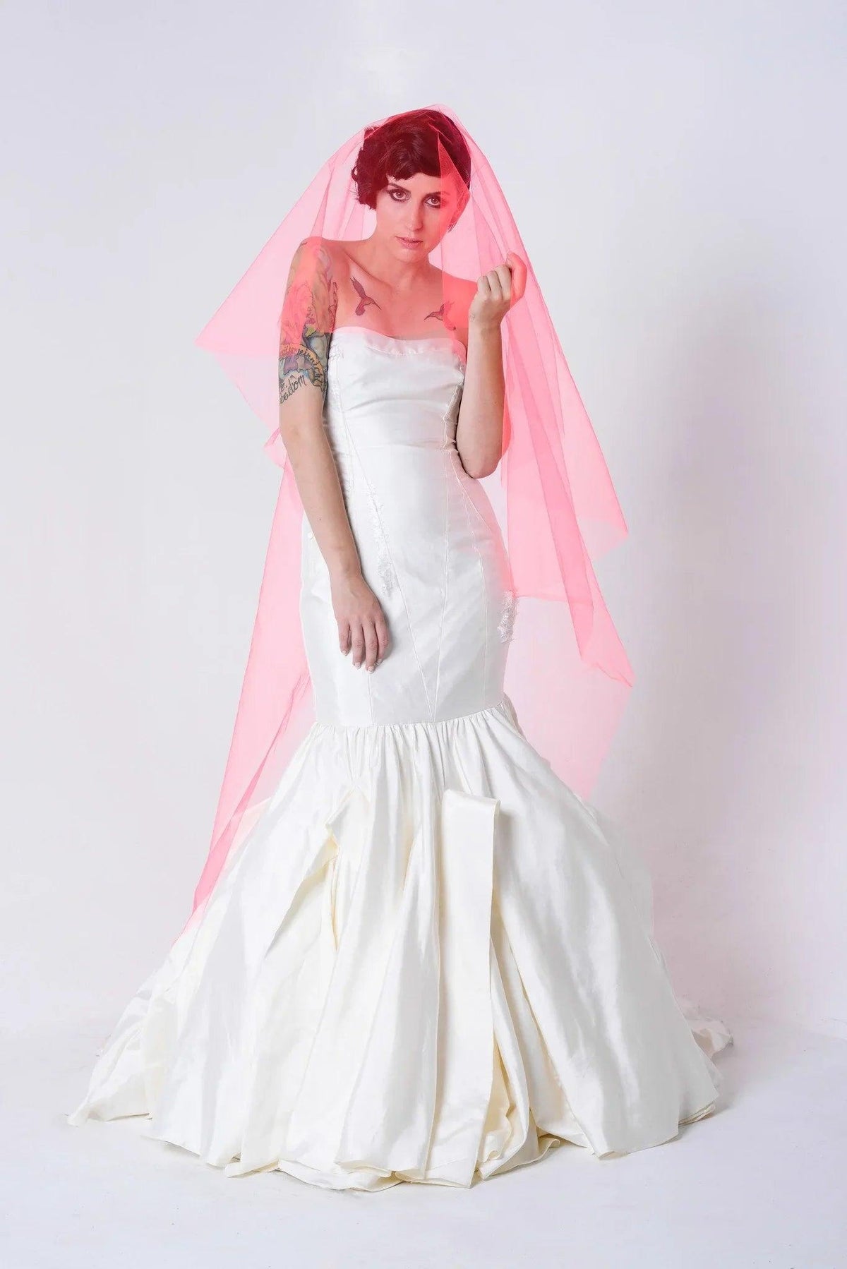 Bride in white mermaid wedding dress with pink veil, showcasing custom bridal design for unique celebrations.