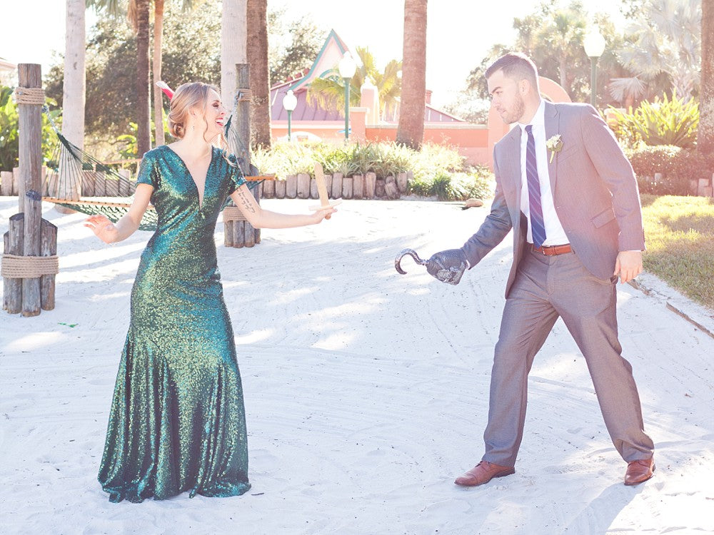 Bride in emerald sequin wedding dress playfully dueling groom with hook on sandy beach