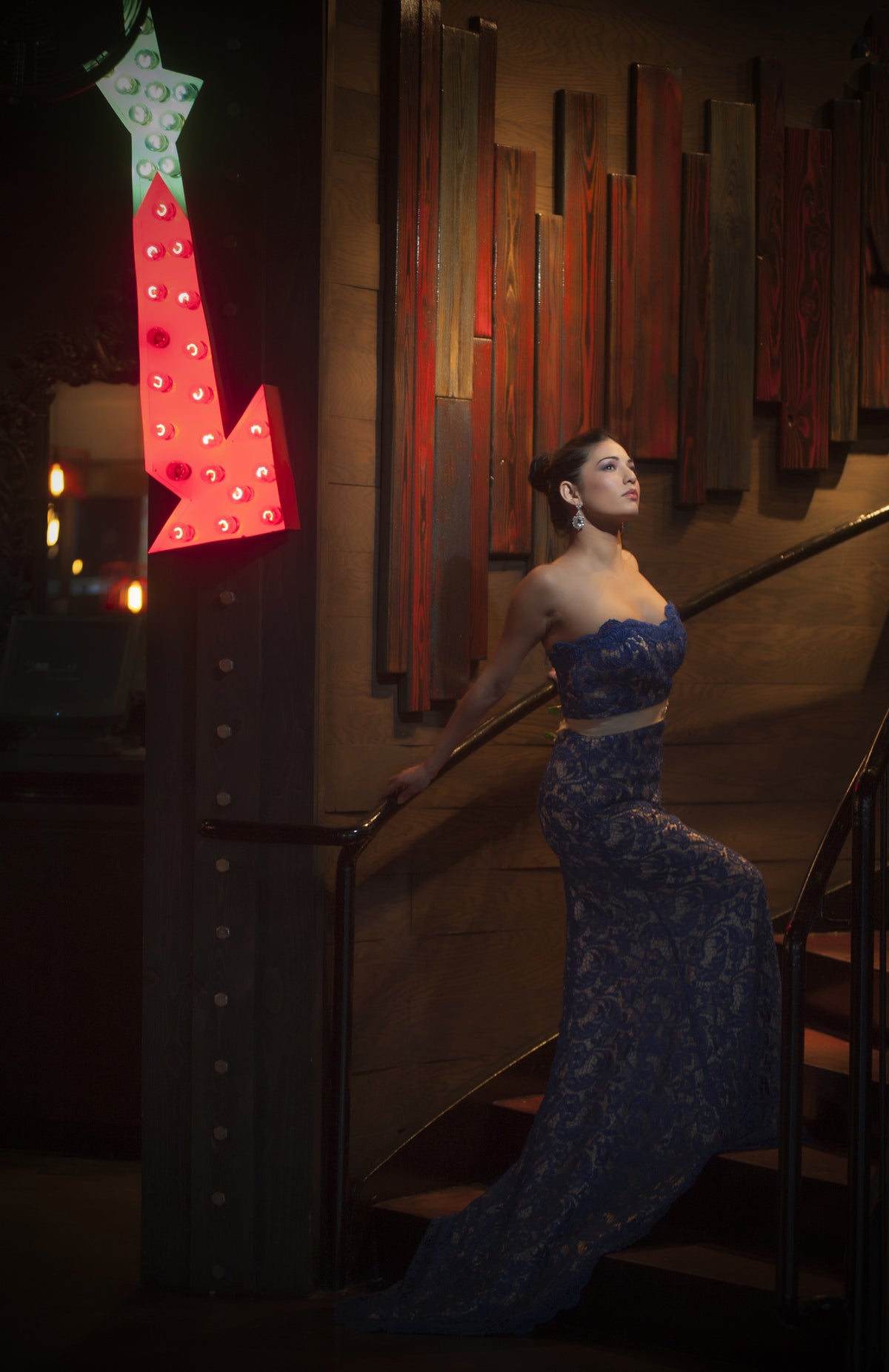 Woman in navy lace strapless wedding gown on staircase beside red neon arrow, luxury bridal design