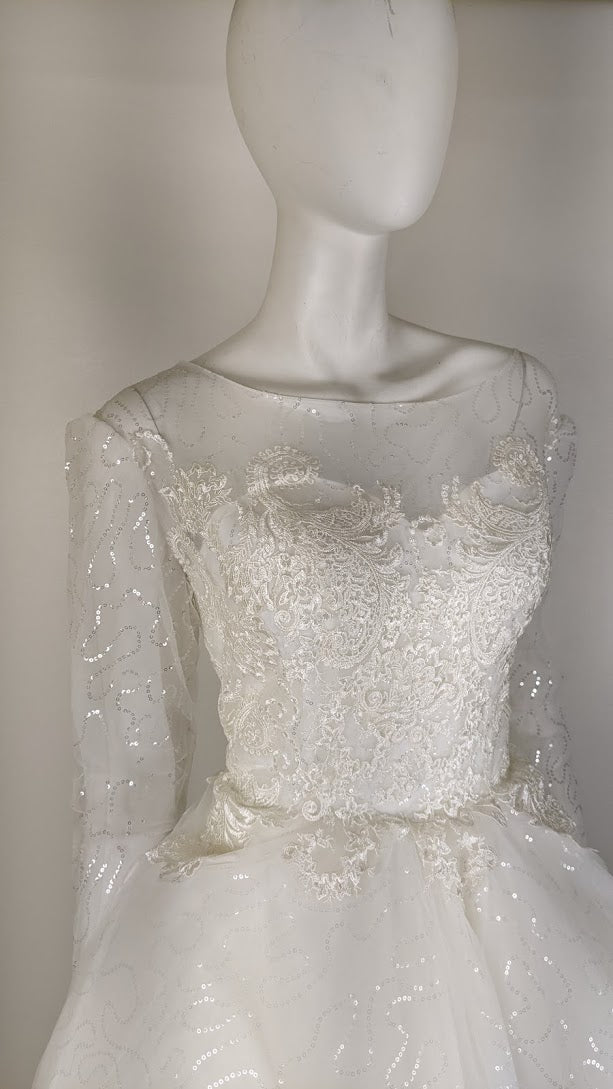 Elegant white wedding dress with lace and sequins, featuring long sleeves and a fitted bodice.
