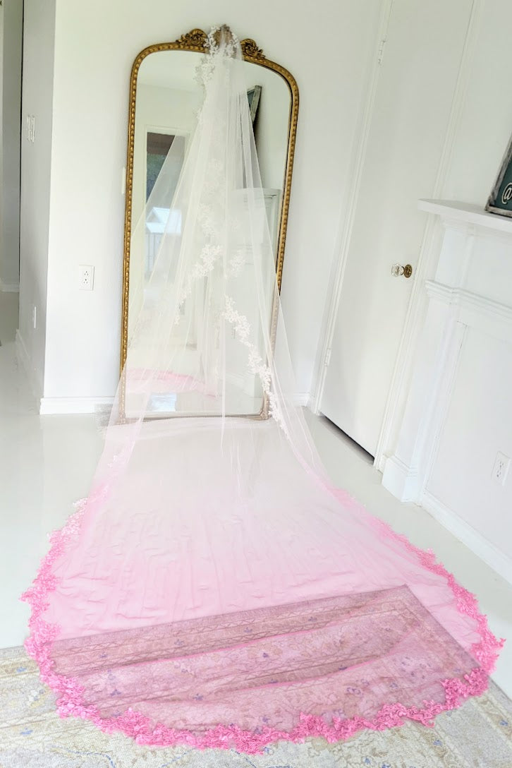 Pink ombre wedding veil with lace trim, displayed on floor near gold mirror