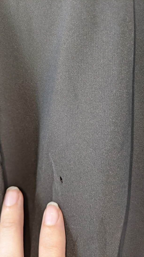 Close-up of dark fabric with small hole, fingers pointing to damage