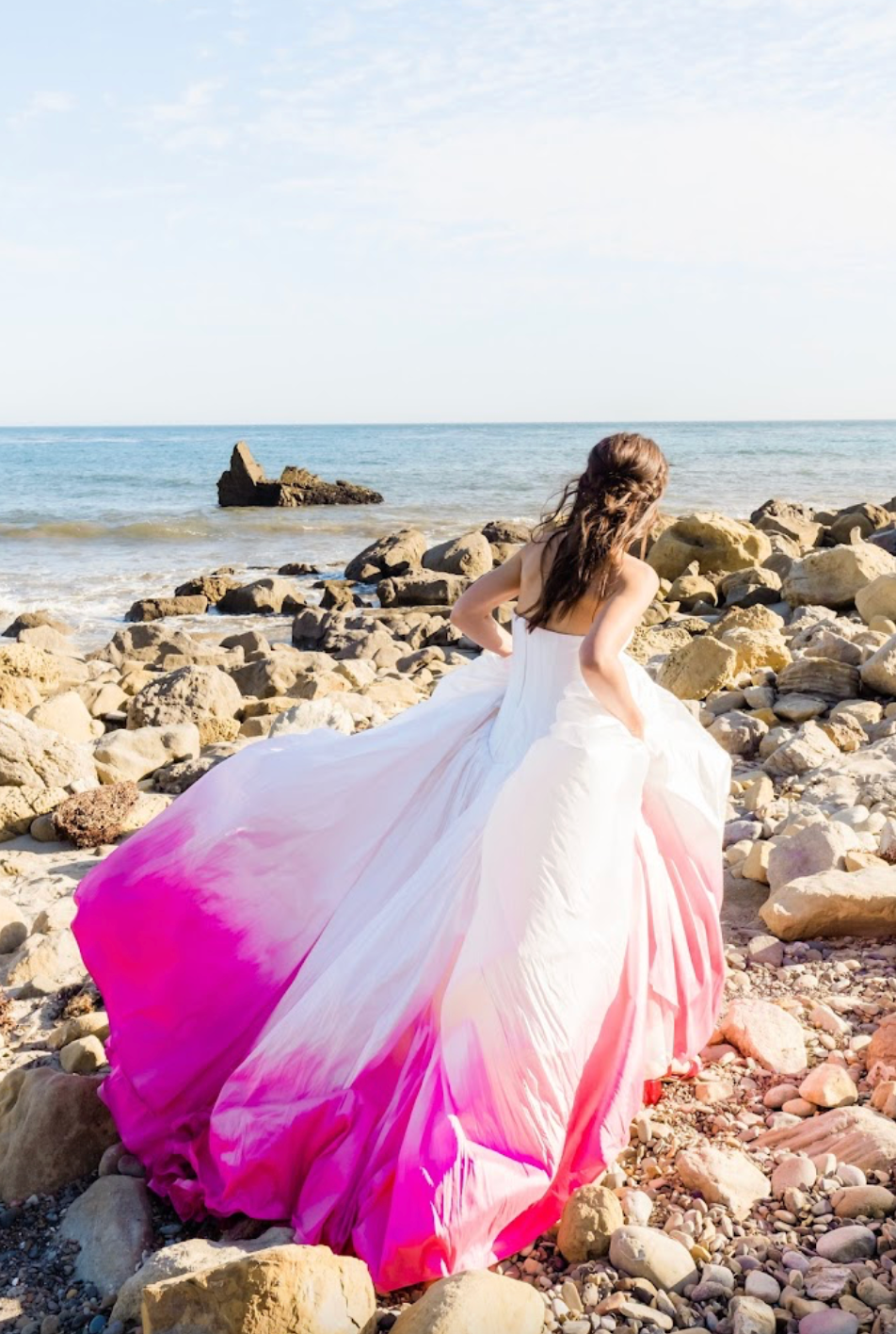 Bride in ombre pink wedding dress on rocky beach, custom dyed gown for unique celebrations