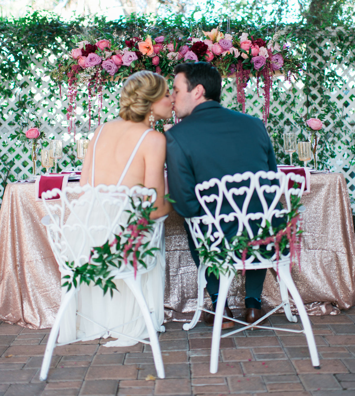 Bride and groom sharing a kiss at a romantic wedding reception with floral decor and rose gold tablecloth.