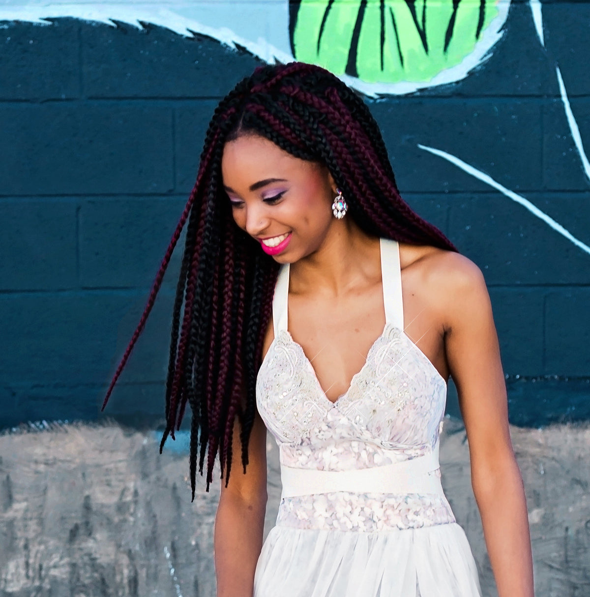 Bride in lace wedding dress with halter neckline, styled with burgundy and black braids, against graffiti wall