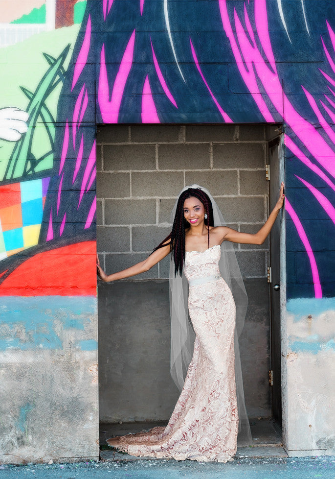 Bride in lace wedding dress with veil, standing in doorway against vibrant mural wall