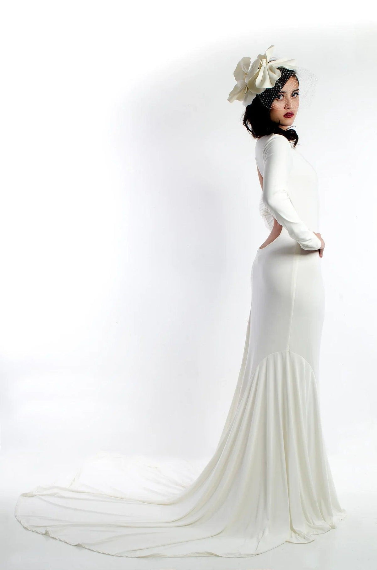 Elegant white wedding dress with long sleeves, open back, and flowing train, paired with a floral veil.