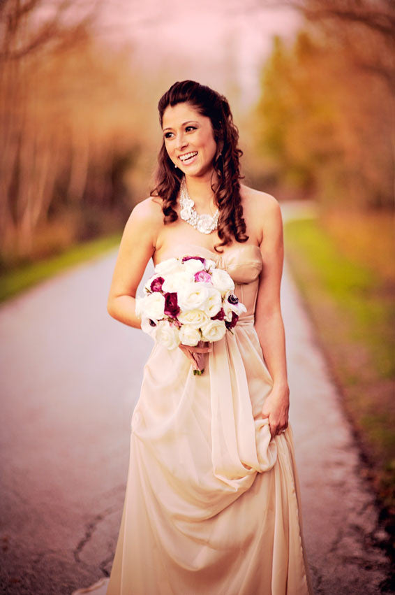 Bride in elegant strapless wedding dress holding bouquet on scenic path