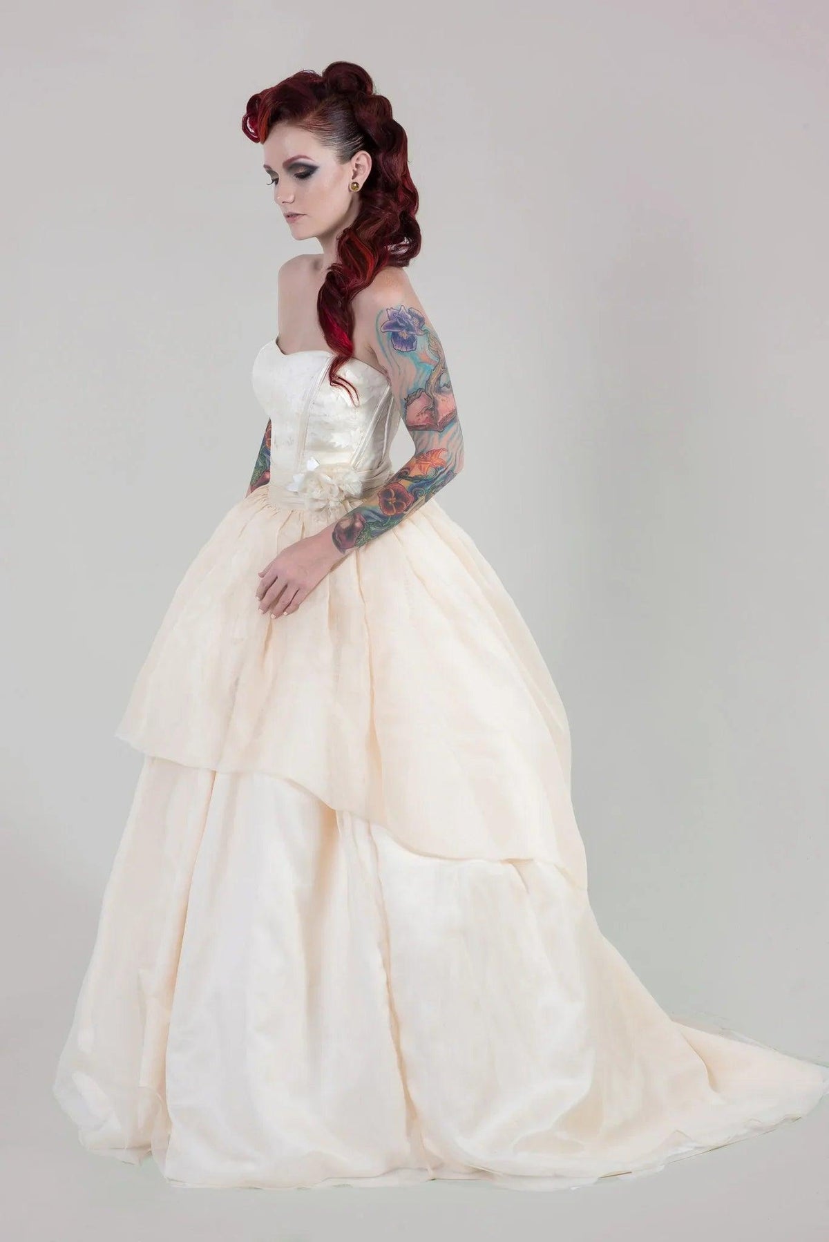 Tattooed bride in strapless ivory wedding gown with tiered skirt, red hair, and floral arm tattoos