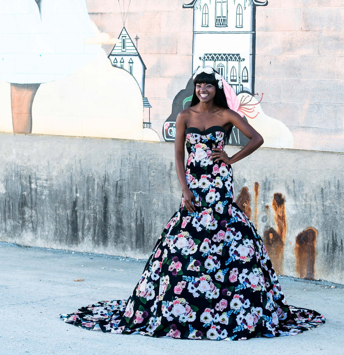 Black floral strapless wedding dress with full skirt, worn by smiling bride against mural backdrop