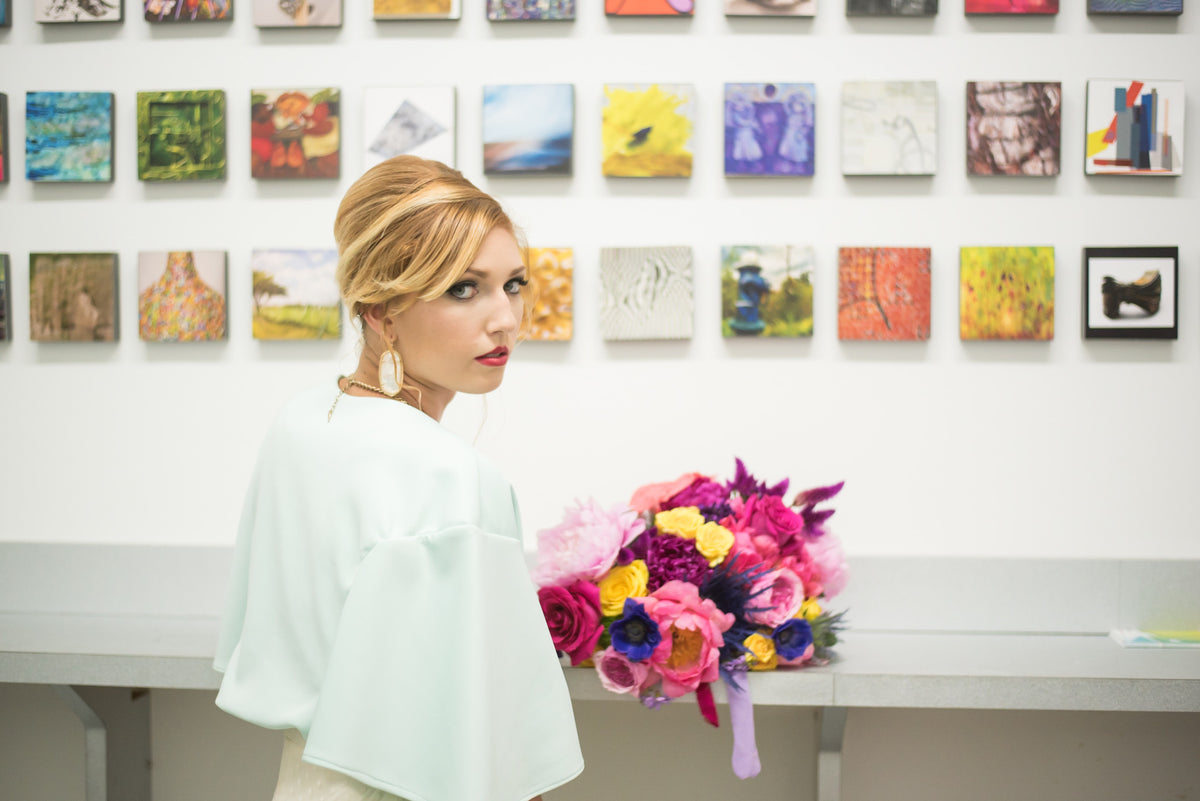 Bride in mint cape with vibrant bouquet, art gallery backdrop, custom wedding dress design