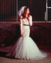 Bride in lace mermaid wedding dress with tulle skirt, black belt, and veil, styled for edgy bridal look