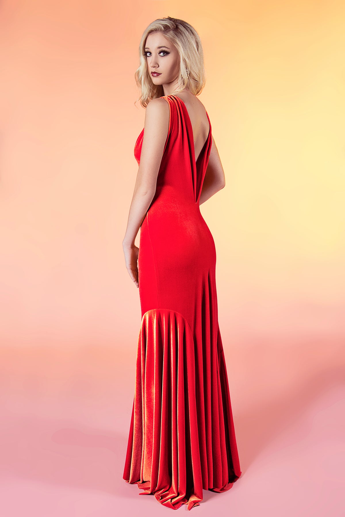 Bold red velvet wedding dress with open back and pleated skirt, perfect for non-traditional brides.