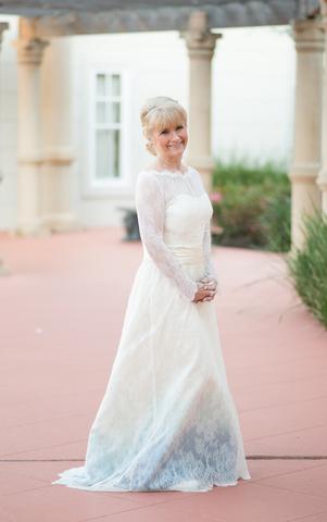 Bride in custom ombre wedding dress with lace sleeves, standing under garden pergola