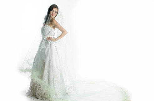 Elegant white wedding dress with flowing veil and soft green accents, perfect for custom bridal designs.